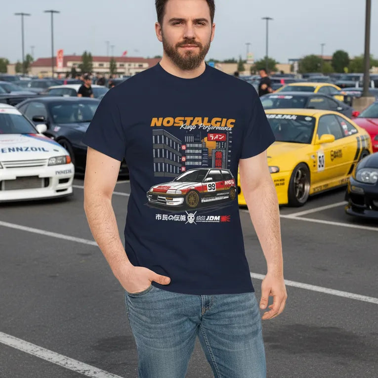 A man wearing a navy blue vintage-style JDM streetwear t-shirt featuring a classic Honda Civic car graphic with "Nostalgic" text, standing in a car lot.