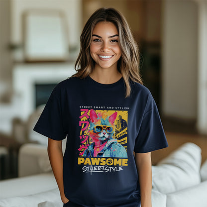 A smiling woman with long brown hair wearing a navy blue Pawsome Cat Graphic Tee. She is standing in a brightly lit indoor space with a blurred living room background, showcasing the oversized fit of the t-shirt.